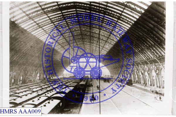 [AAA009] Aloft view through train shed toward country end. Several lines of carriages left. Hanging lamps. pl