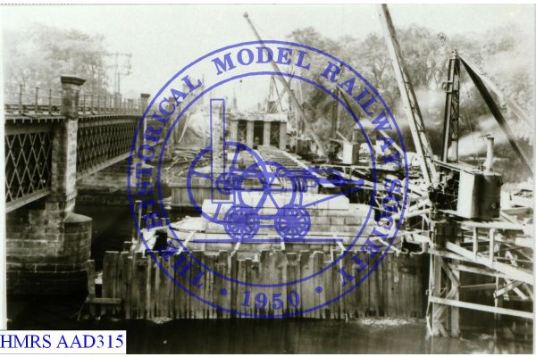 [AAD315] Viaduct under construction across river beside completed viaduct. Steam cranes used in contruction.